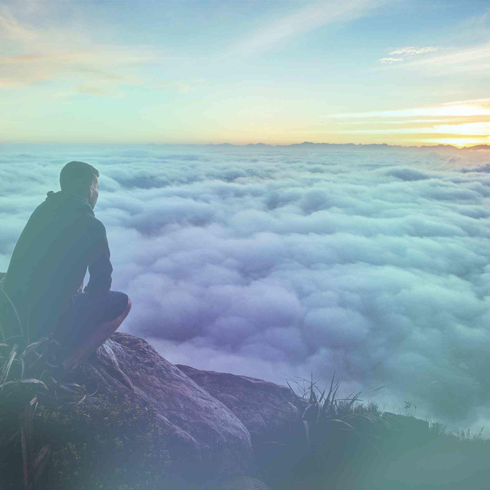 Man auf grauem Felsen blickt auf Wolken unter sich im Sonnenaufgang